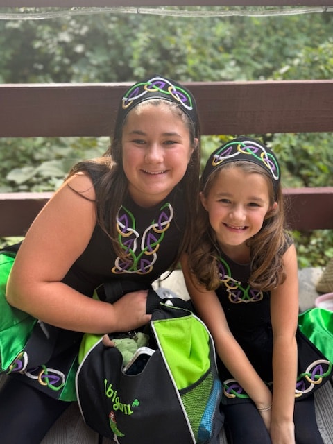 Two young dancers in black Celtic Irish dance costumes and decorative headbands posing outdoors