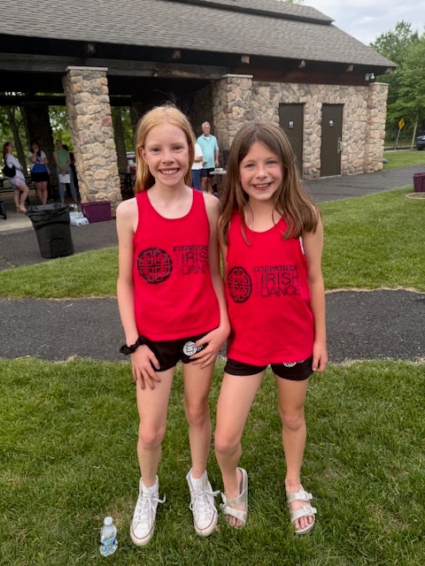 Two young dancers in black Celtic Irish dance costumes and headbands posing outdoors