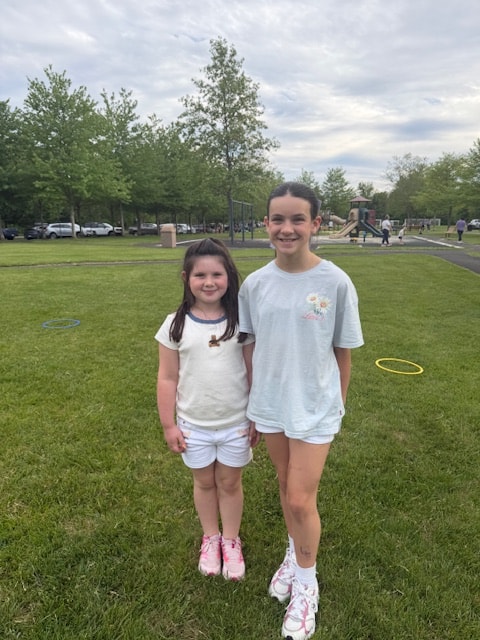 Two young dancers in black Celtic Irish dance costumes sitting together outdoors