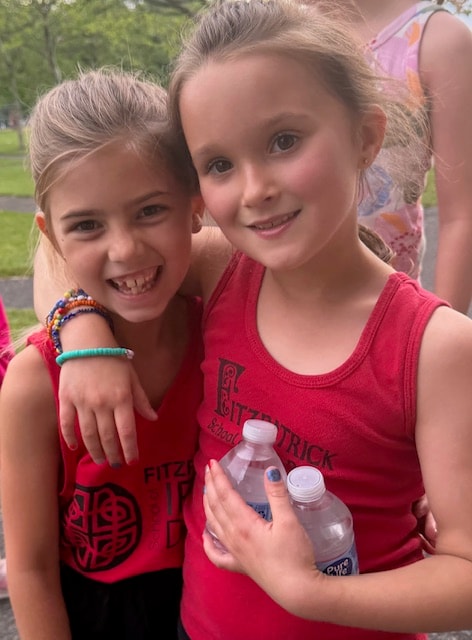 Two young dancers in matching floral jumpsuits smiling at a park