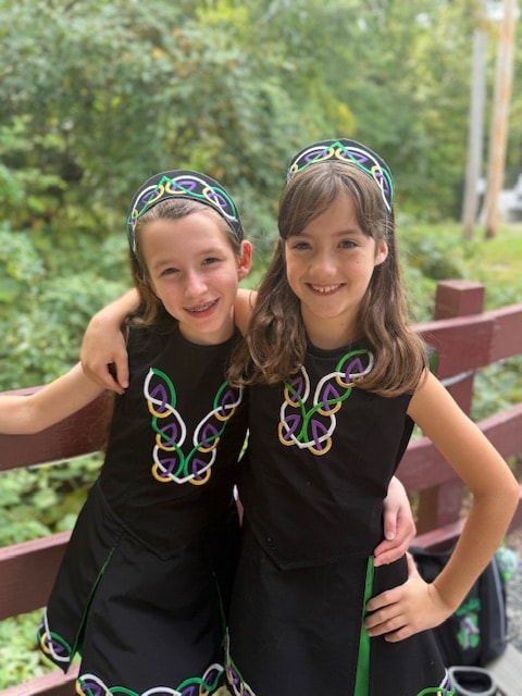 Two young dancers in red Fitzpatrick Irish Dance shirts smiling outdoors
