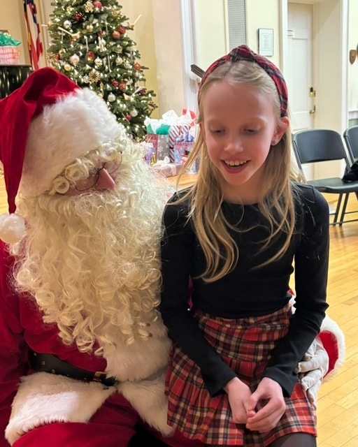 Young Fitzpatrick dancer in plaid headband and skirt sitting with Santa Claus at the holiday party