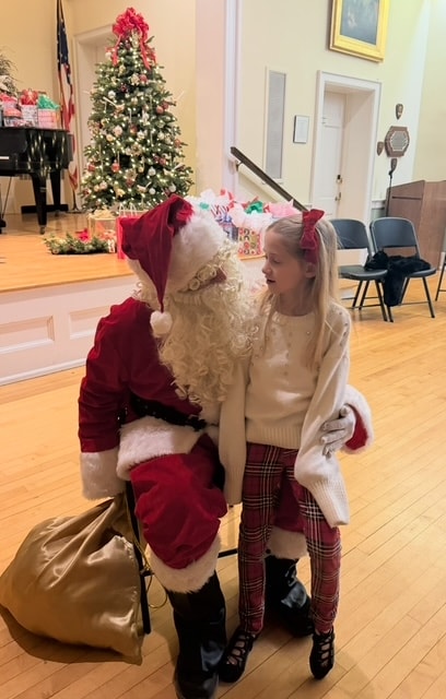 Young dancer in plaid pants and white top whispering to Santa Claus at the holiday party