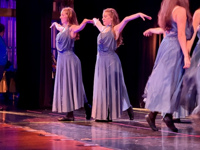 Group of dancers in grey gowns on stage with aurora borealis backdrop