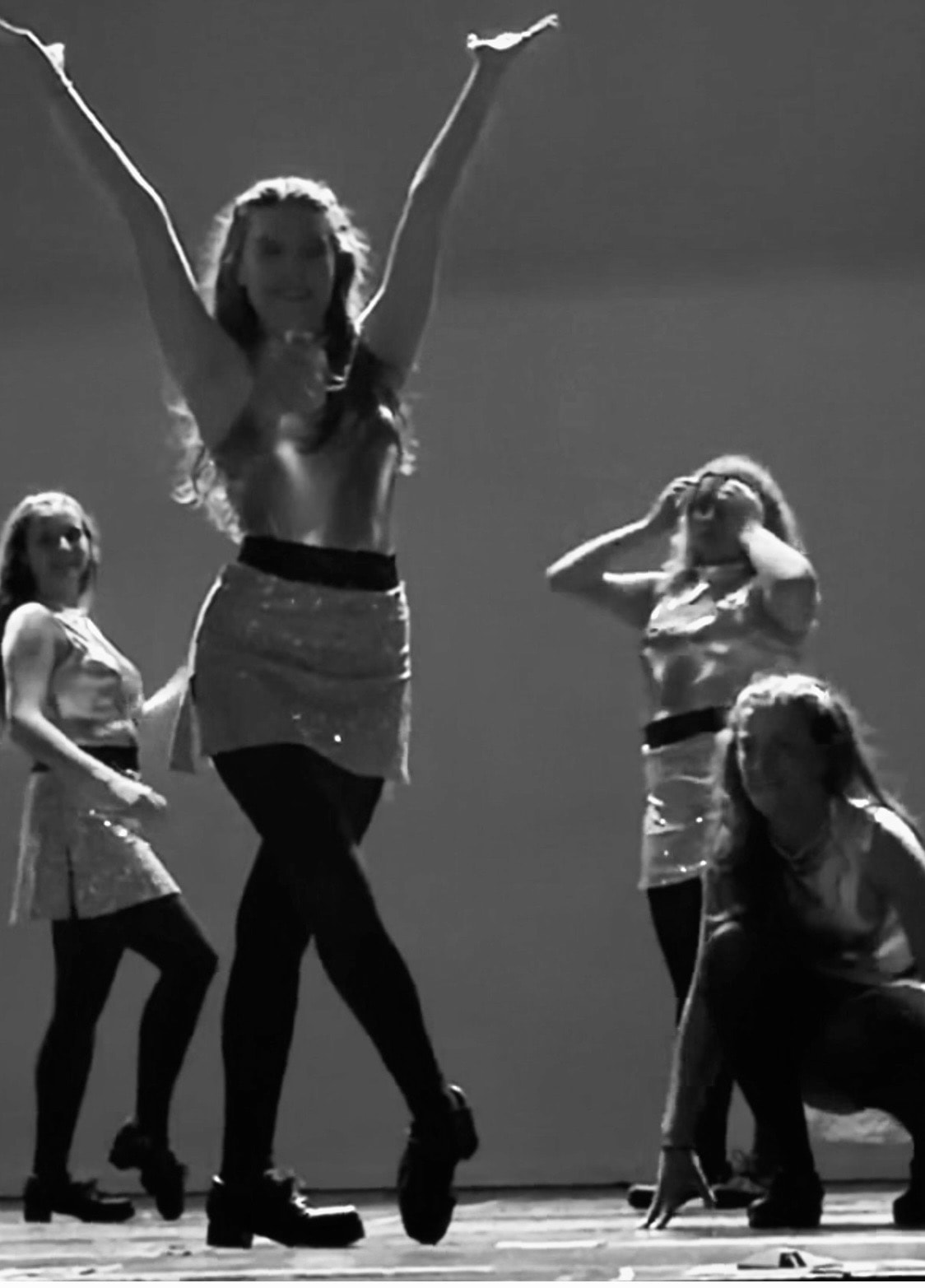 Dancer with arms raised on stage surrounded by ensemble, black and white performance photo