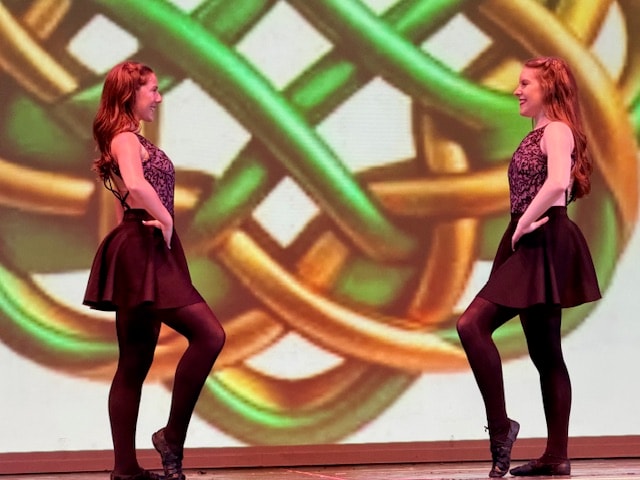 Two dancers performing in front of a Celtic knot backdrop
