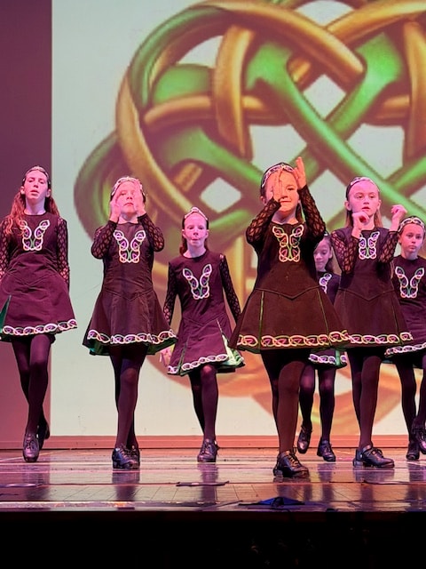 Group of young dancers in traditional Irish costumes with Celtic knot backdrop