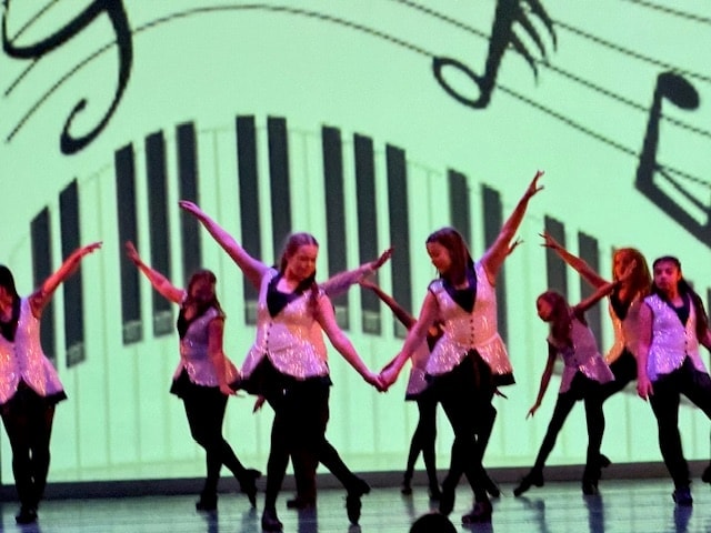 Group of dancers performing on stage with musical notes backdrop