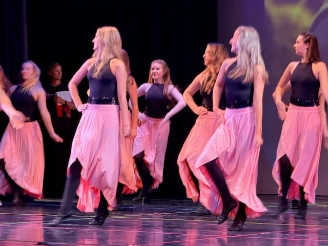 Adult dancers in black tops and flowing pink skirts performing on stage