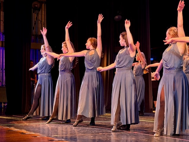 Two dancers in flowing purple gowns performing on stage with arms extended