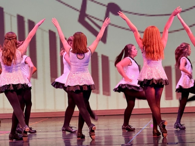 Fitzpatrick dancers in teal tops and dark skirts performing close together on stage