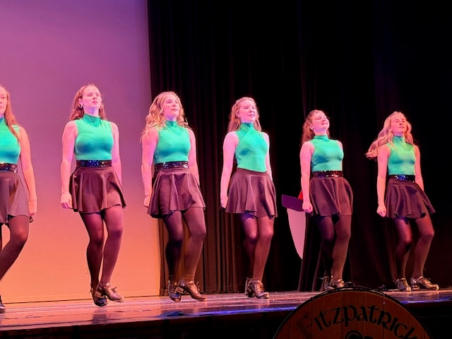 Fitzpatrick dancers in teal tops performing with Ireland flag backdrop