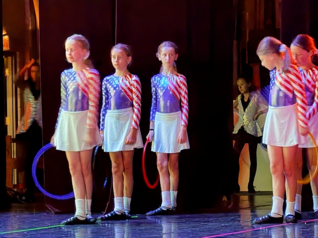 Four young dancers in USA flag costumes holding colorful hoops on stage