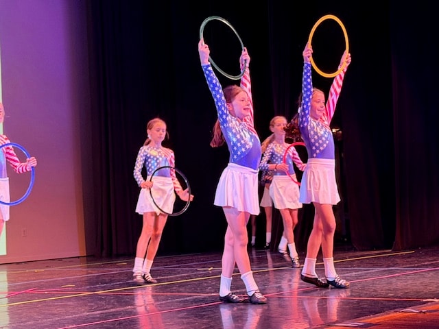 Young dancers in USA costumes holding hula hoops on stage