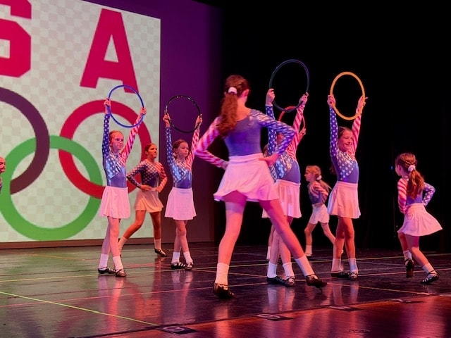 Group of dancers in USA costumes with Olympic rings backdrop and hula hoops
