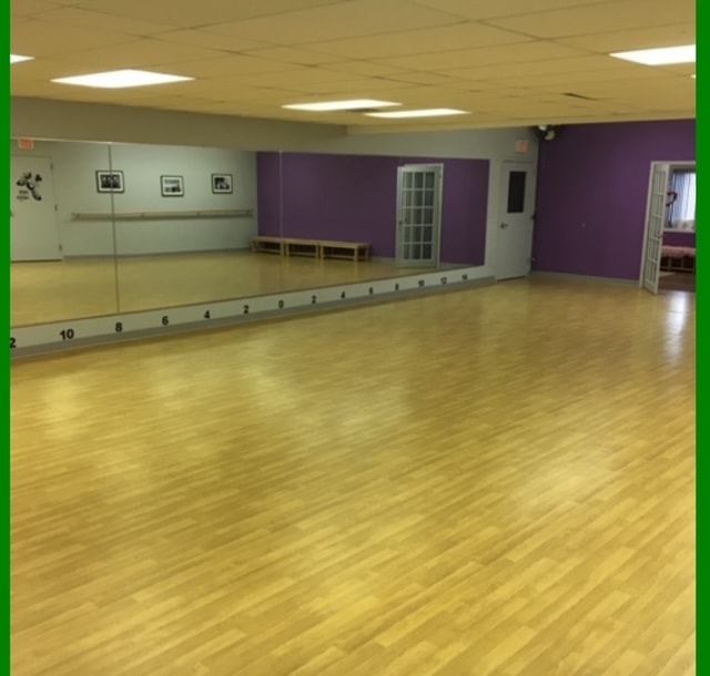Main studio with full-length mirror wall, barre, and hardwood floor